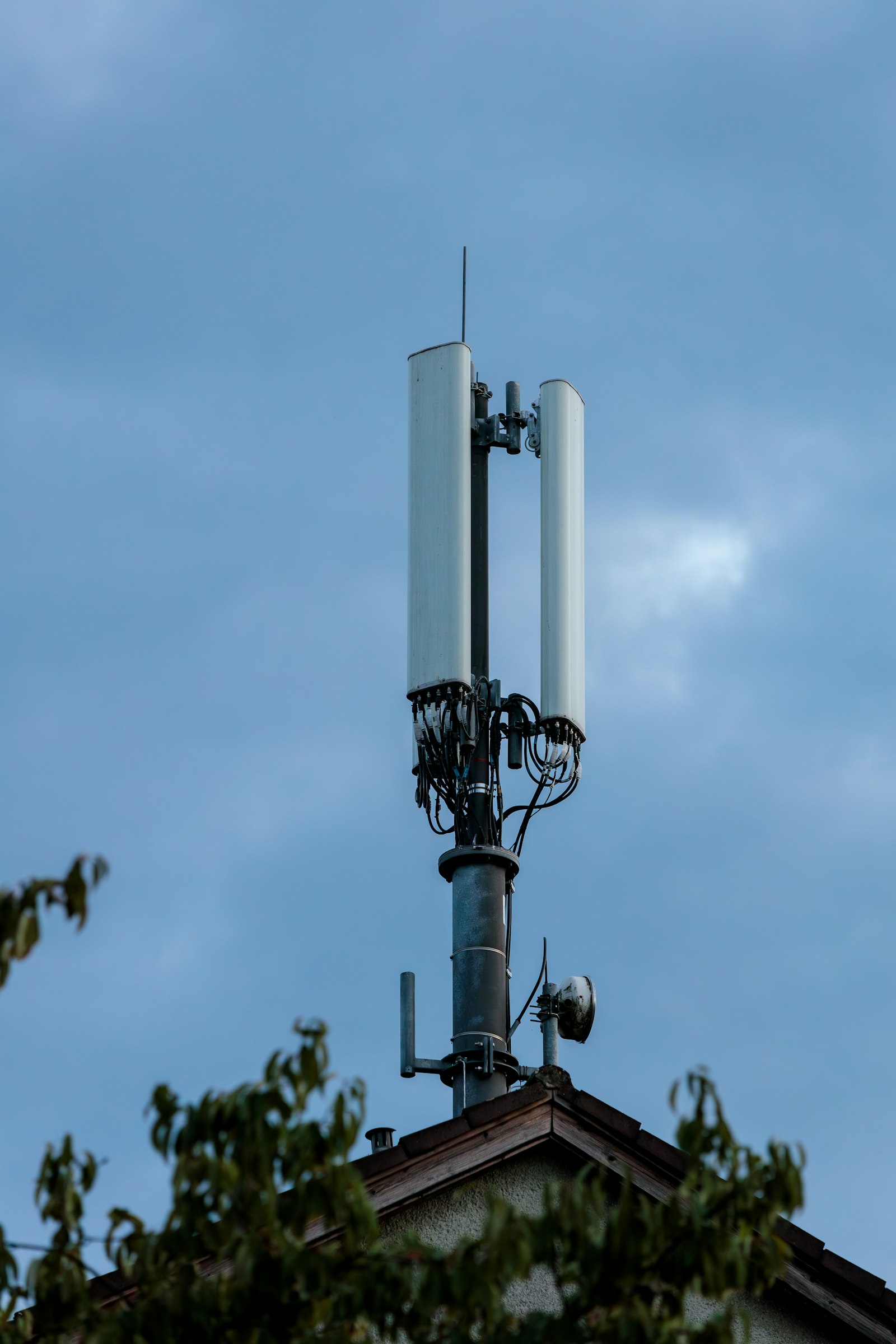 A cell phone tower antenna installation on a rooftop against a blue sky, illustrating telecom network infrastructure