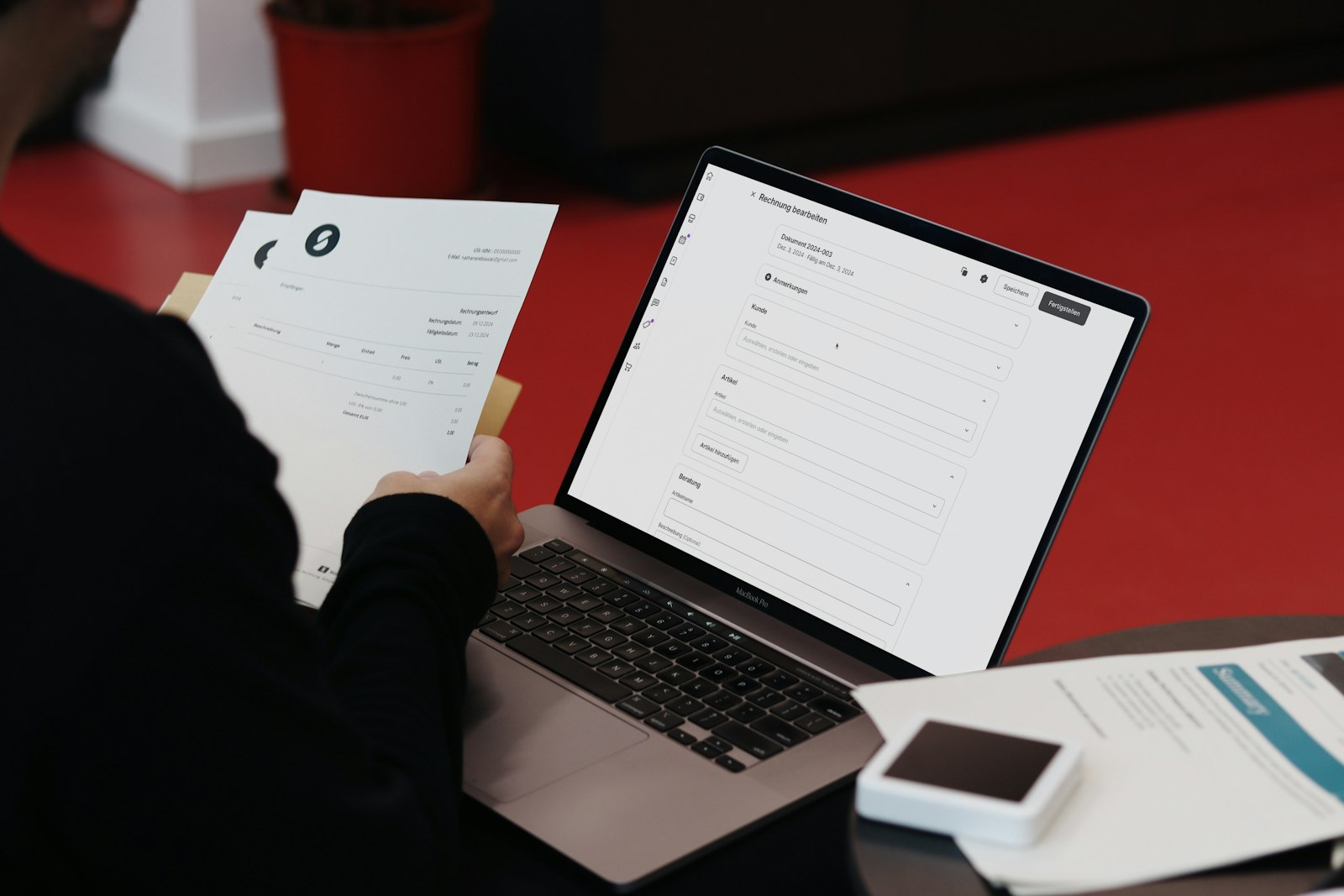 A person reconciling printed paper documents against an online invoice system at an office desk