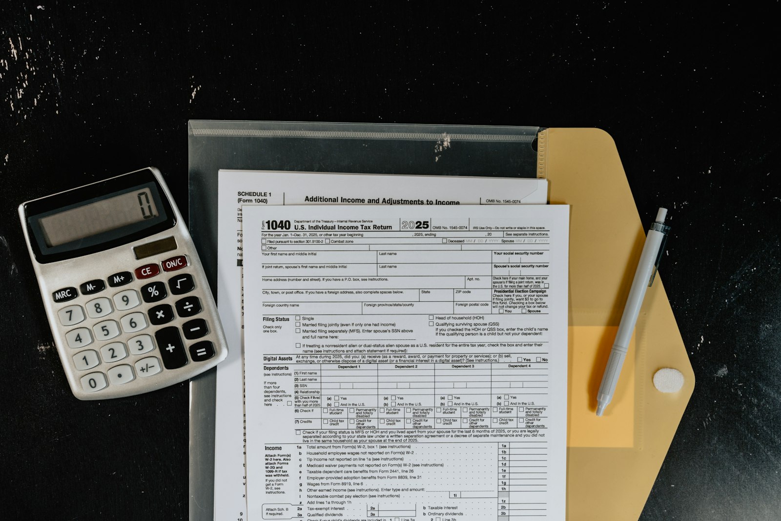 A calculator resting on printed tax and payroll forms on a dark desk surface