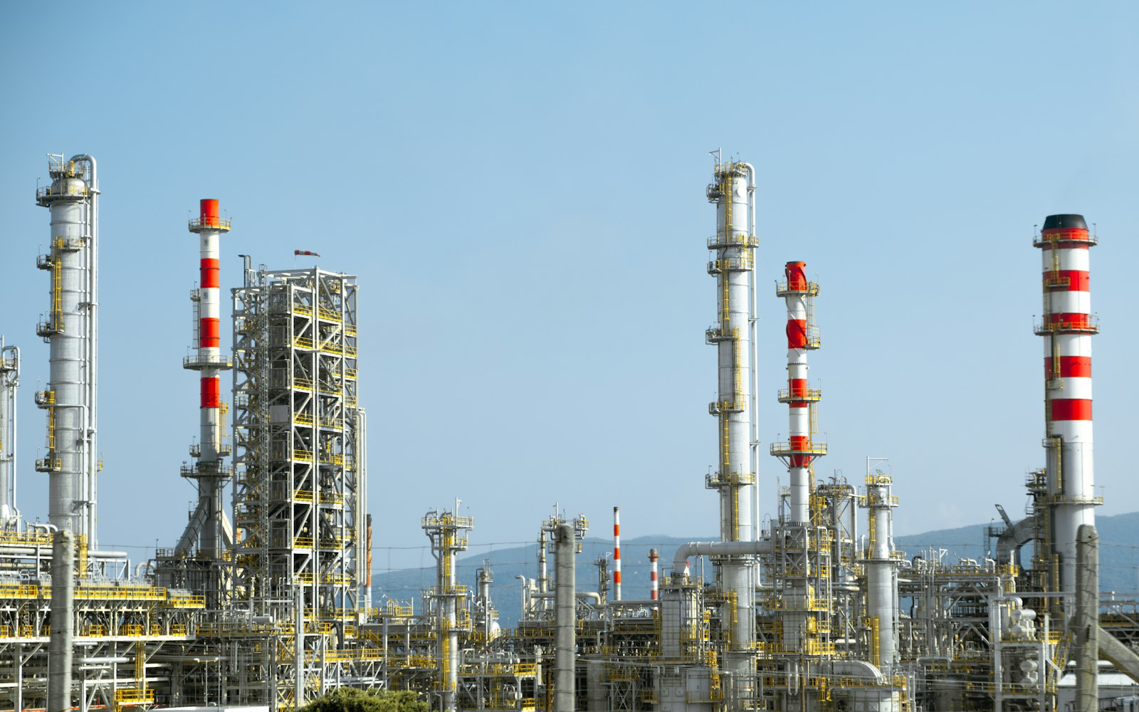 Network of red and white pipes at an oil and gas processing facility under daylight