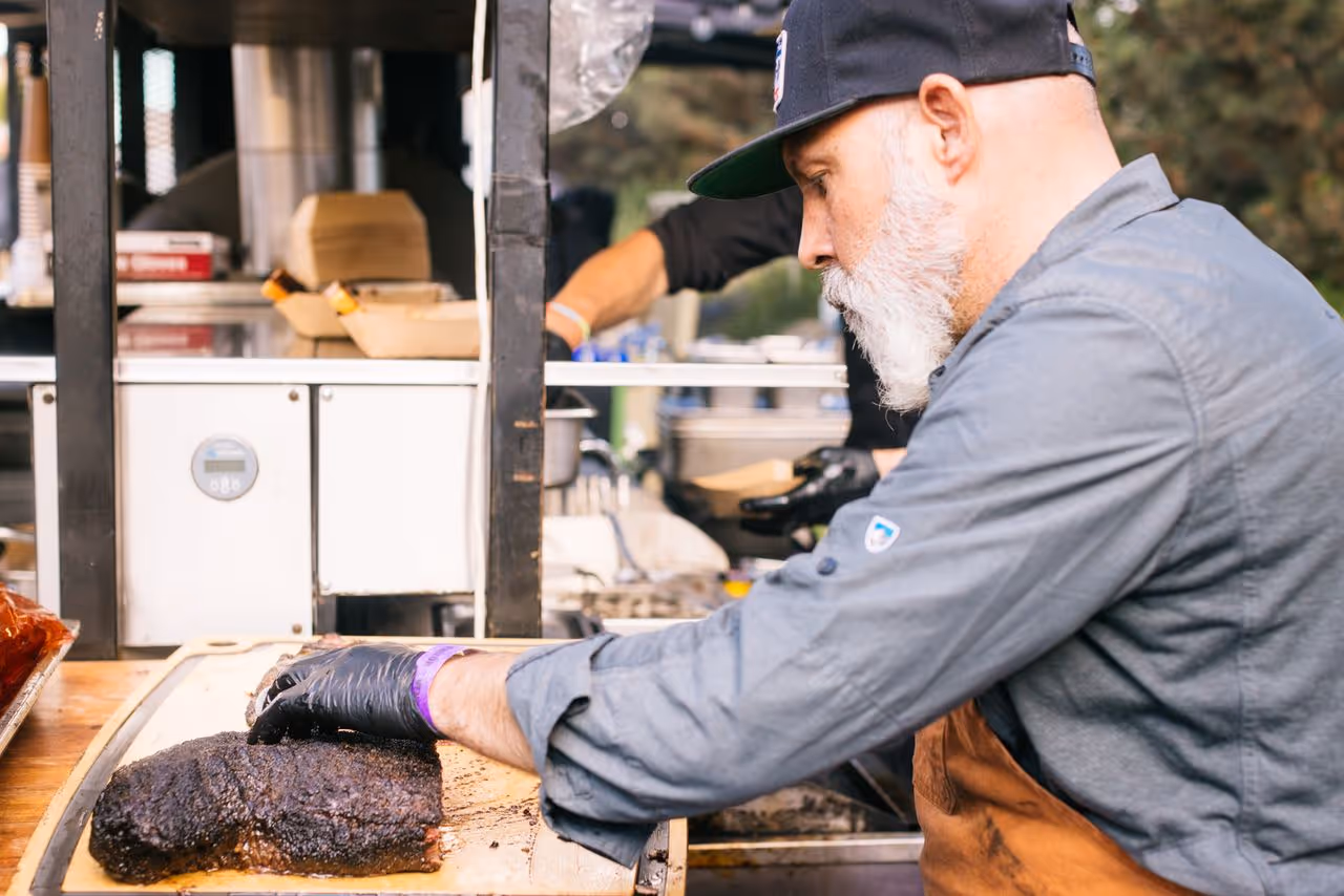 A man with a beard and a hat is cooking meat.