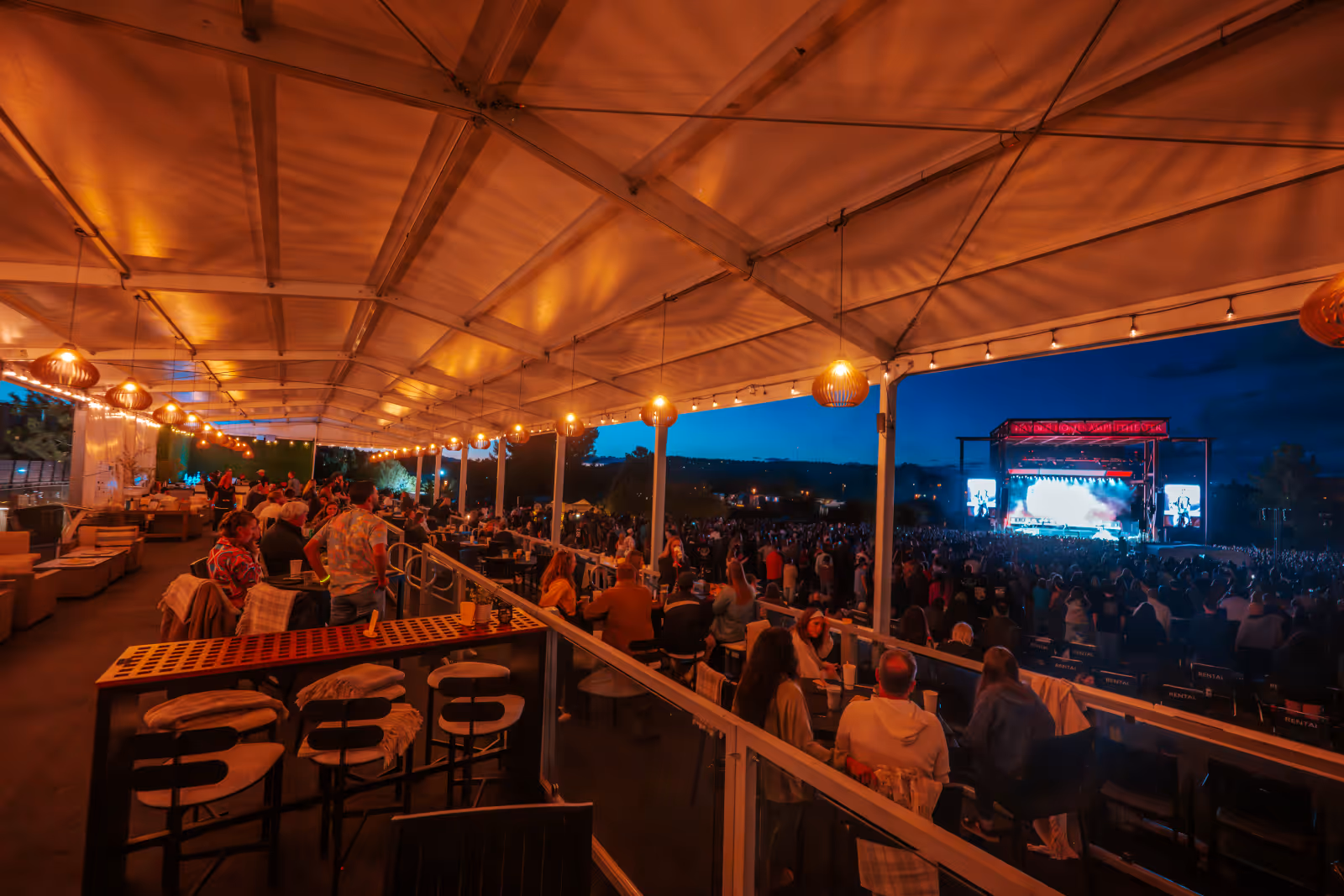 Crowd watching a nighttime outdoor concert at Hayden Homes Amphitheater with covered seating area.