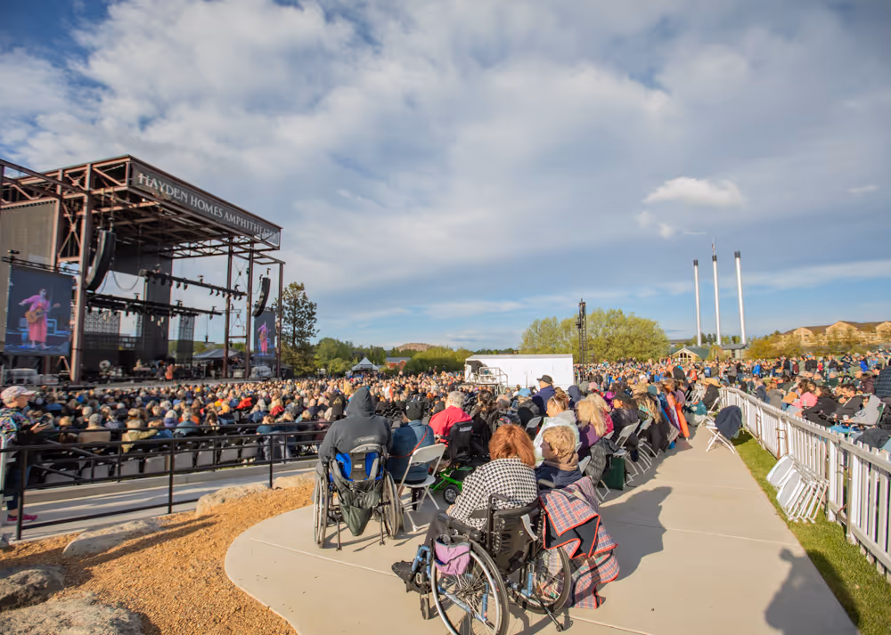 Outdoor concert at Hayden Homes Amphitheater with audience, some in wheelchairs, on a sunny day.