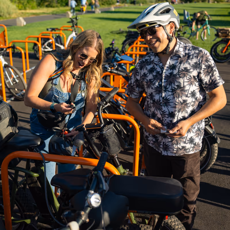 Woman unlocking her bike at a bike rack while a man wearing a helmet watches and smiles.