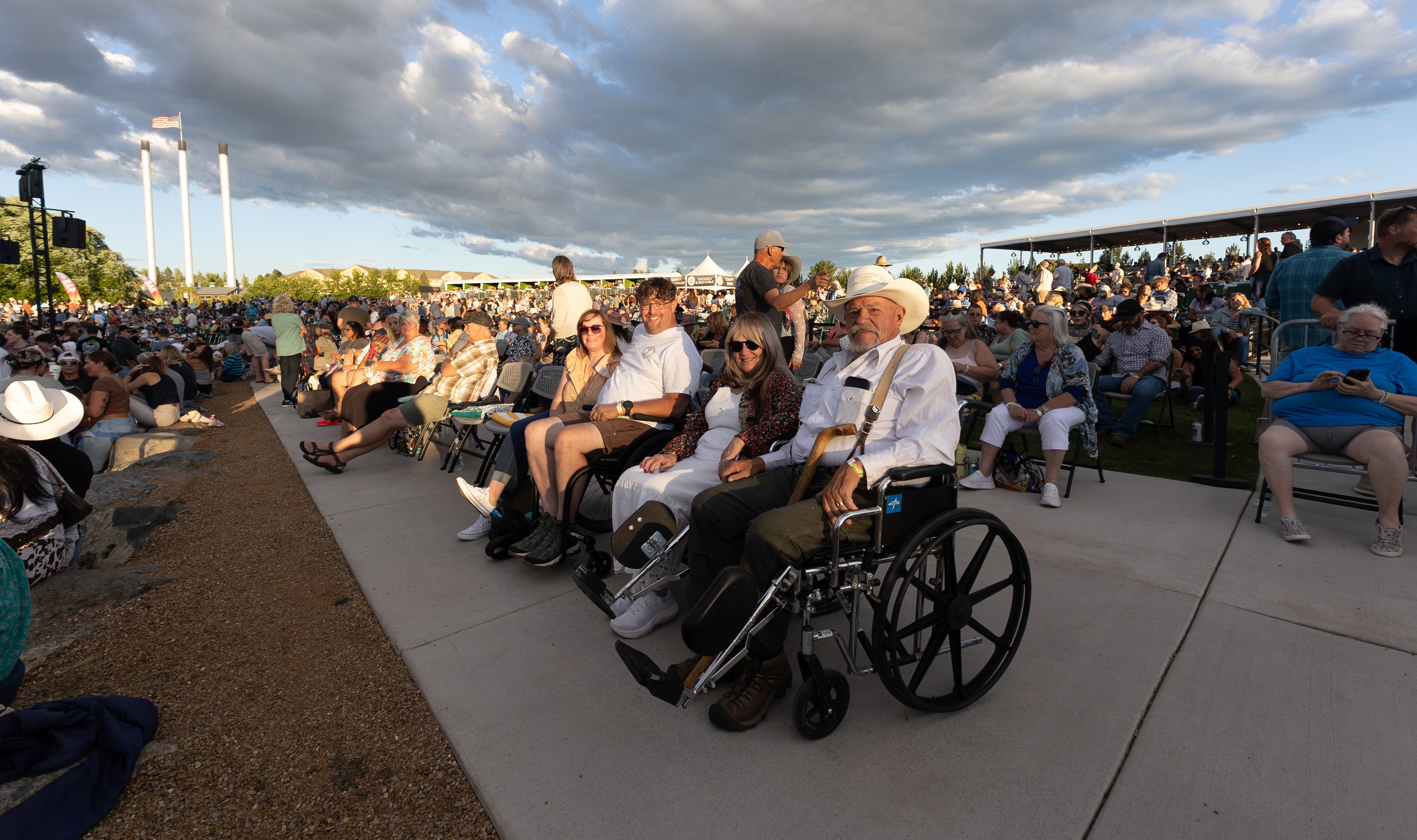 Accessible seating is available at Hayden Homes Amphitheater in Bend, Oregon. Pictured here is a fella with a cowboy hat in a wheelchair sitting with his family in chairs provided by the venue.