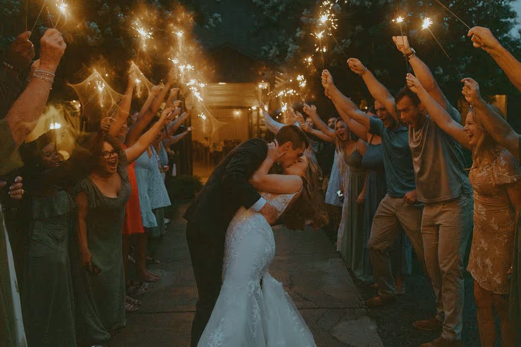 Bride and groom kissing in the center while guests on both sides hold sparklers raised in celebration.