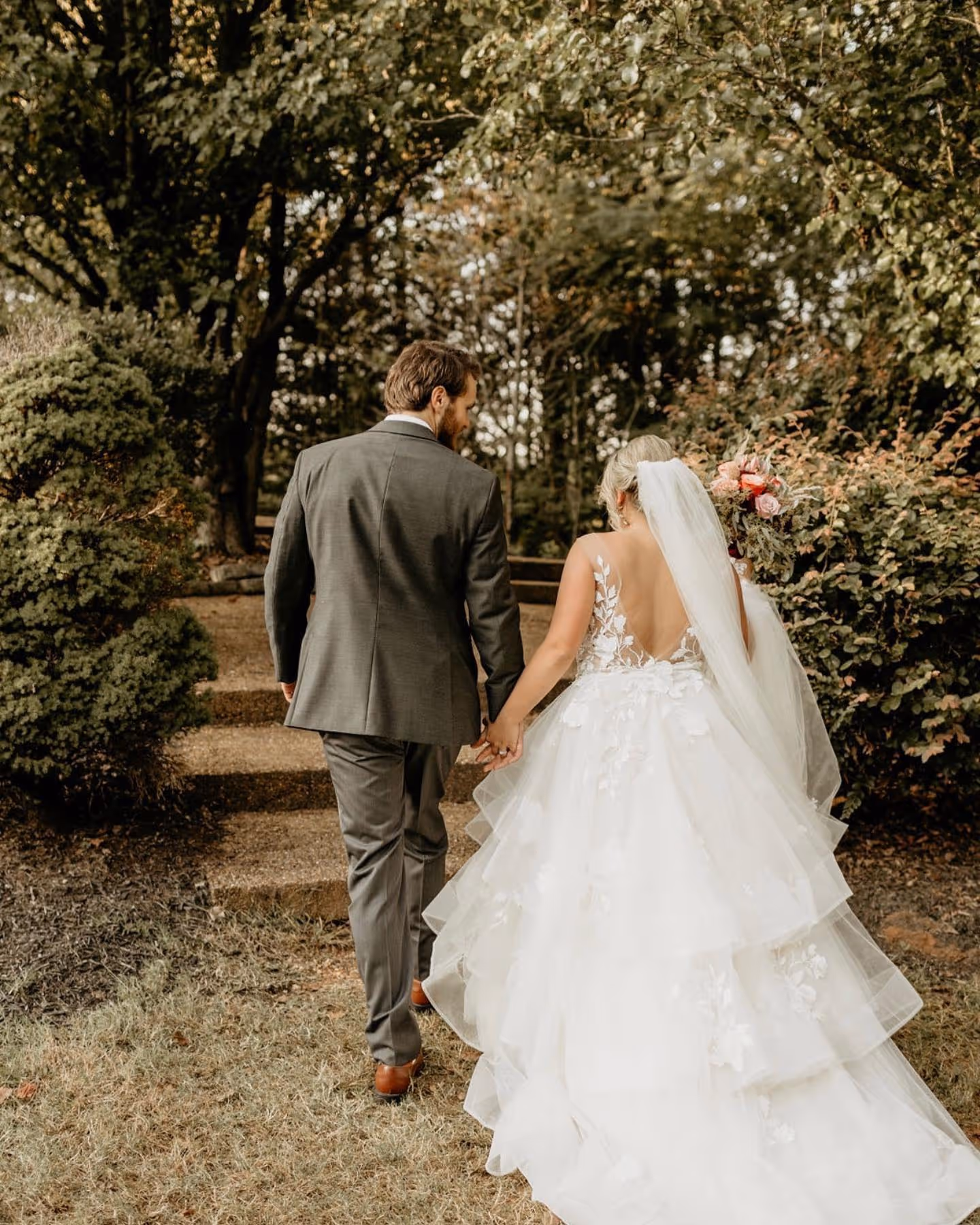 Bride and groom holding hands walking up stone steps surrounded by greenery.