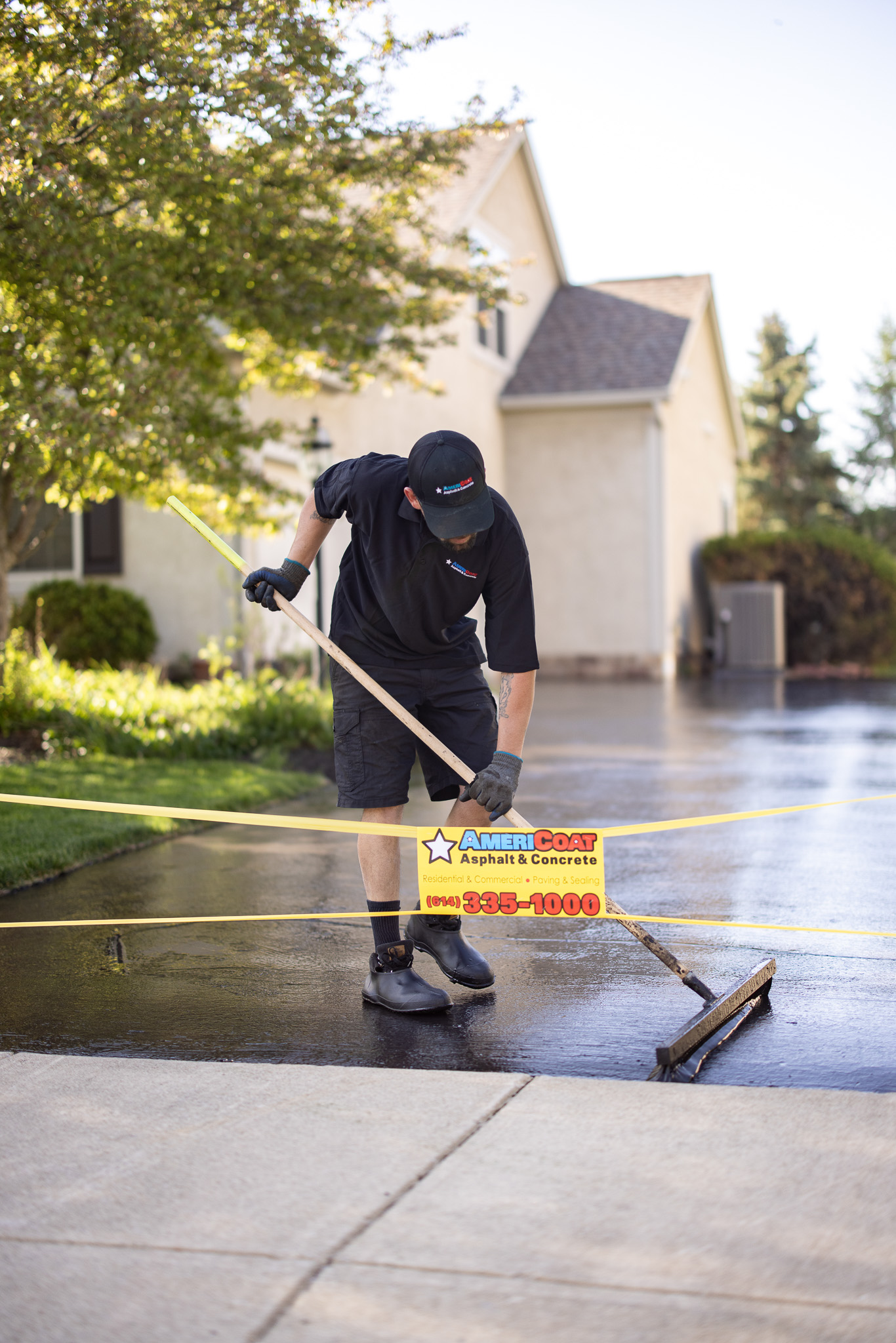 AmeriCoat technician applying asphalt sealcoating with squeegee on residential driveway in Columbus Ohio