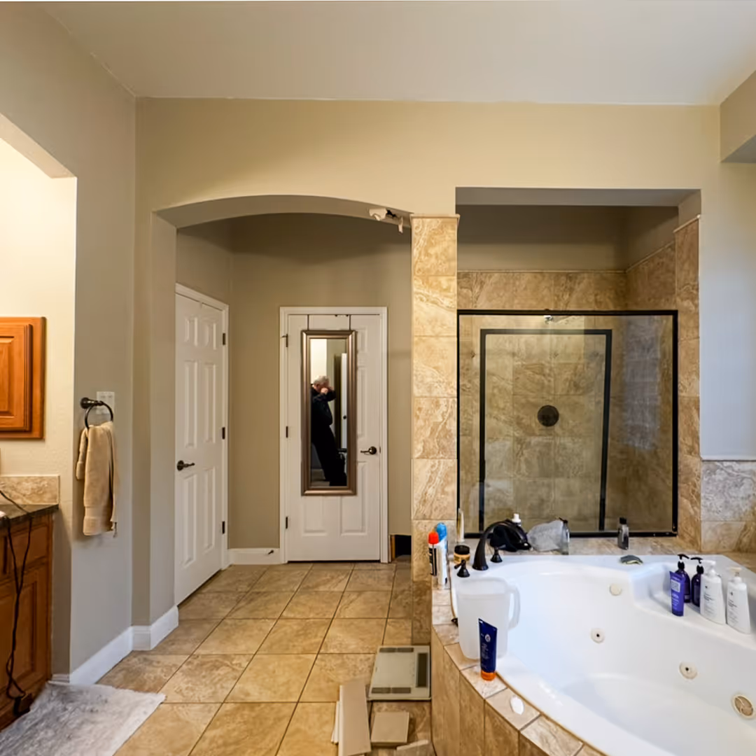 Bathroom before remodeling with large tiled floor, a jacuzzi tub with bath products, a glass-enclosed shower, and a door with a full-length mirror.