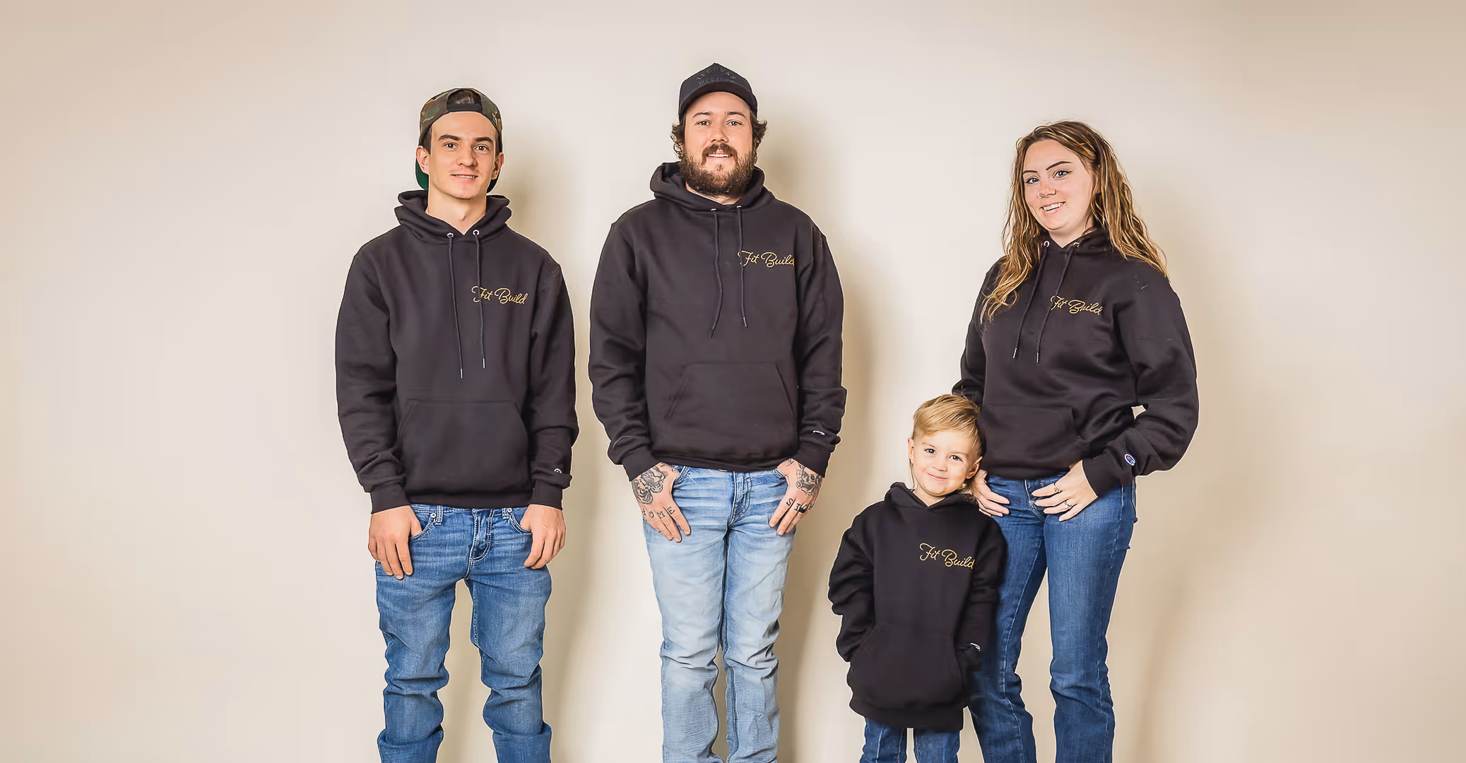 Fit Build team wearing matching black hoodies with 'Fit Build' logo standing against a plain beige wall.