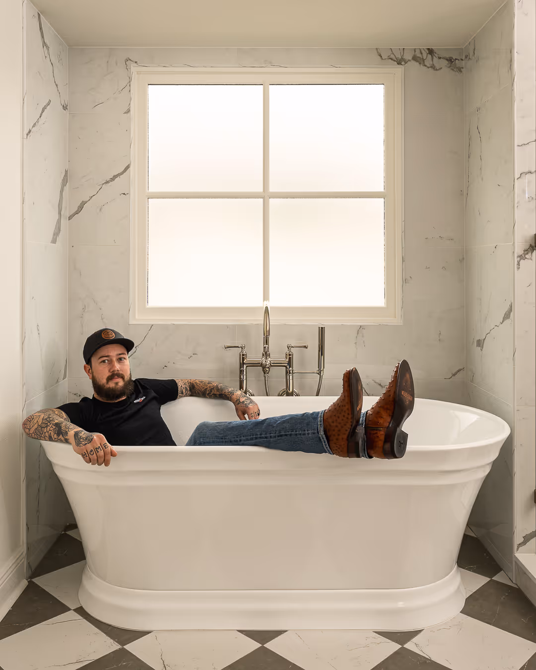 General Contracotor reclining in a white freestanding bathtub in a marble-tiled bathroom, Tarrytown, Austin.