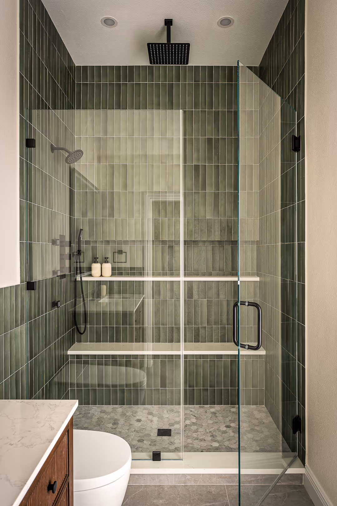 Remodeled Austin modern bathroom shower with vertical green tiles, glass door, overhead rain shower, and hexagonal floor tiles.