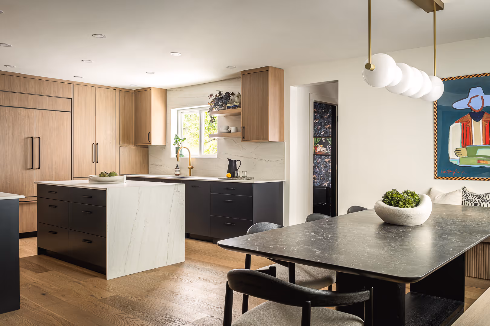 Modern remodeled kitchen with a marble island, wood and black cabinets, dining table with black chairs, and colorful artwork on the wall.
