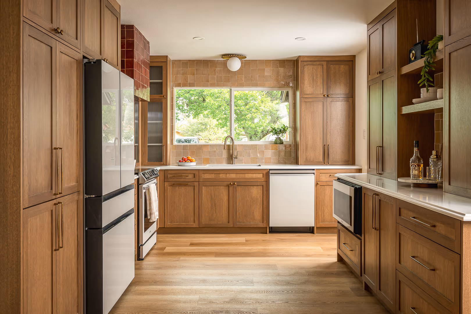 Modern kitchen remodel with wooden cabinets, stainless steel appliances, light wood flooring, and a large window over the sink - South Austin.
