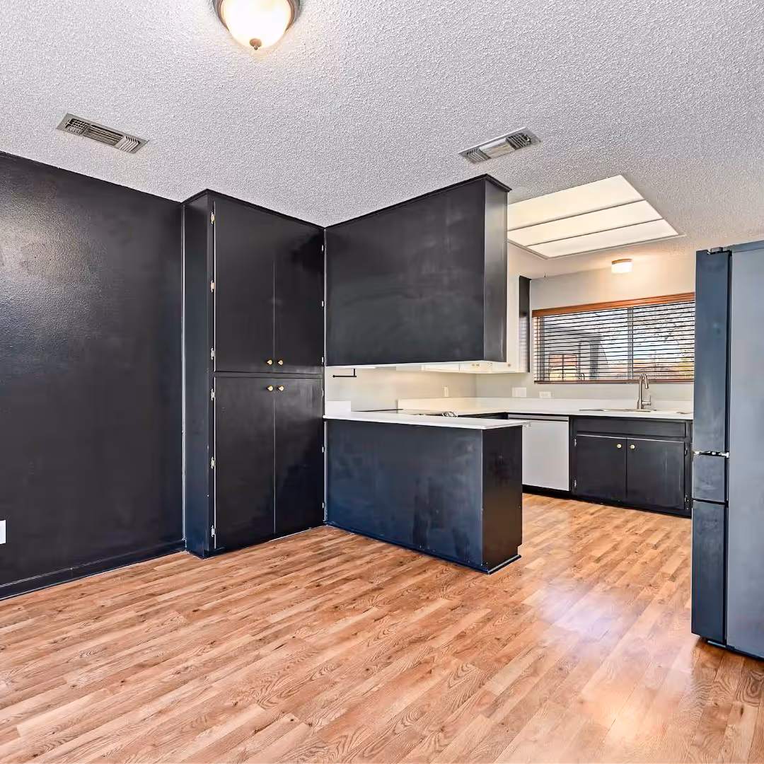Before the remodel: kitchen with black cabinets, white countertops, wood laminate flooring, and a window with blinds.
