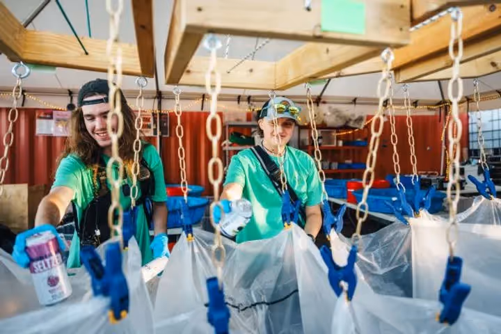 Hayden Homes Amphitheater Green Team members sorting through and recycling cans backstage. The members in the picture are smiling and the operation is backstage