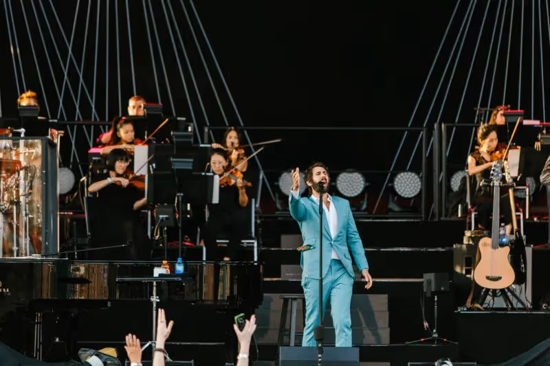 Josh Groban serenading the crowd on an elaborate set with tall stairs and elegant lighting