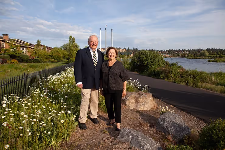 Bill and Trish Smith in the Old Mill District surrounded by wildflowers with the smock stacks in the background