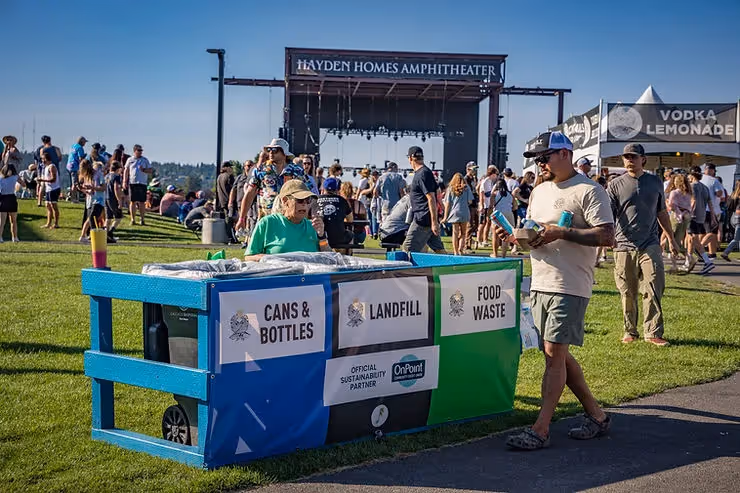 Photo of a waste station in the venue during a show with Green Team staff and Hayden Homes Amphitheater stage in the back.