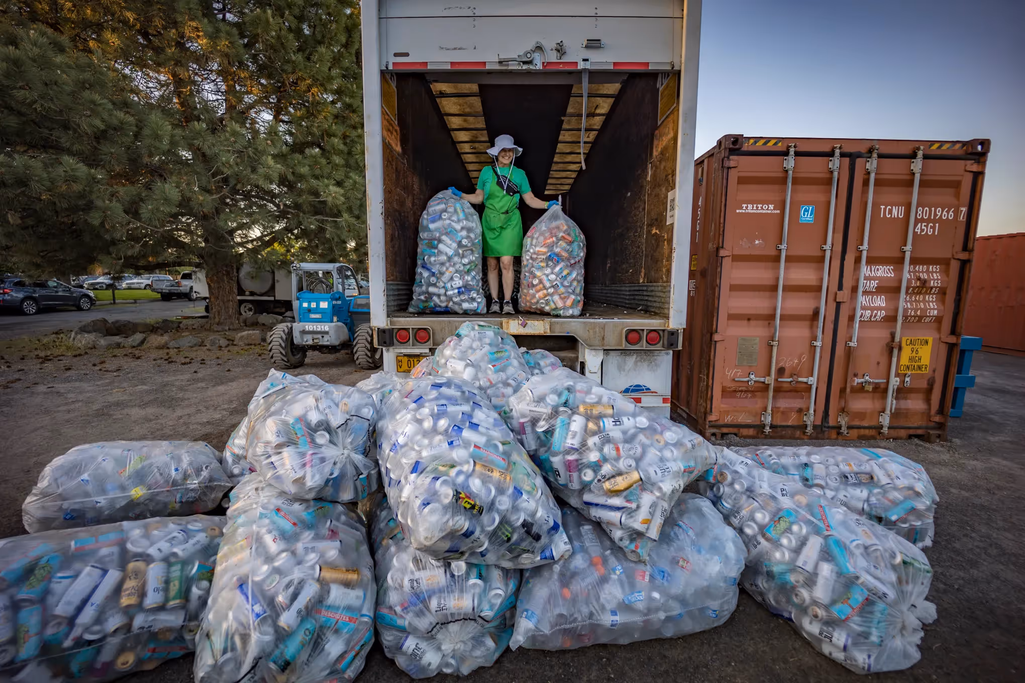 Member of Hayden Homes Amphitheater's Green Team in truck bed in front of a giant pile of cans to be recycled as part of their sustainability efforts.