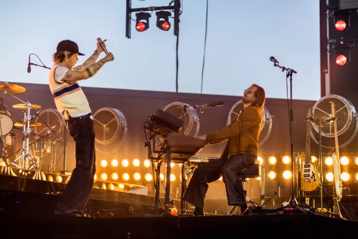 2 people are playing music on stage with a band on the stage