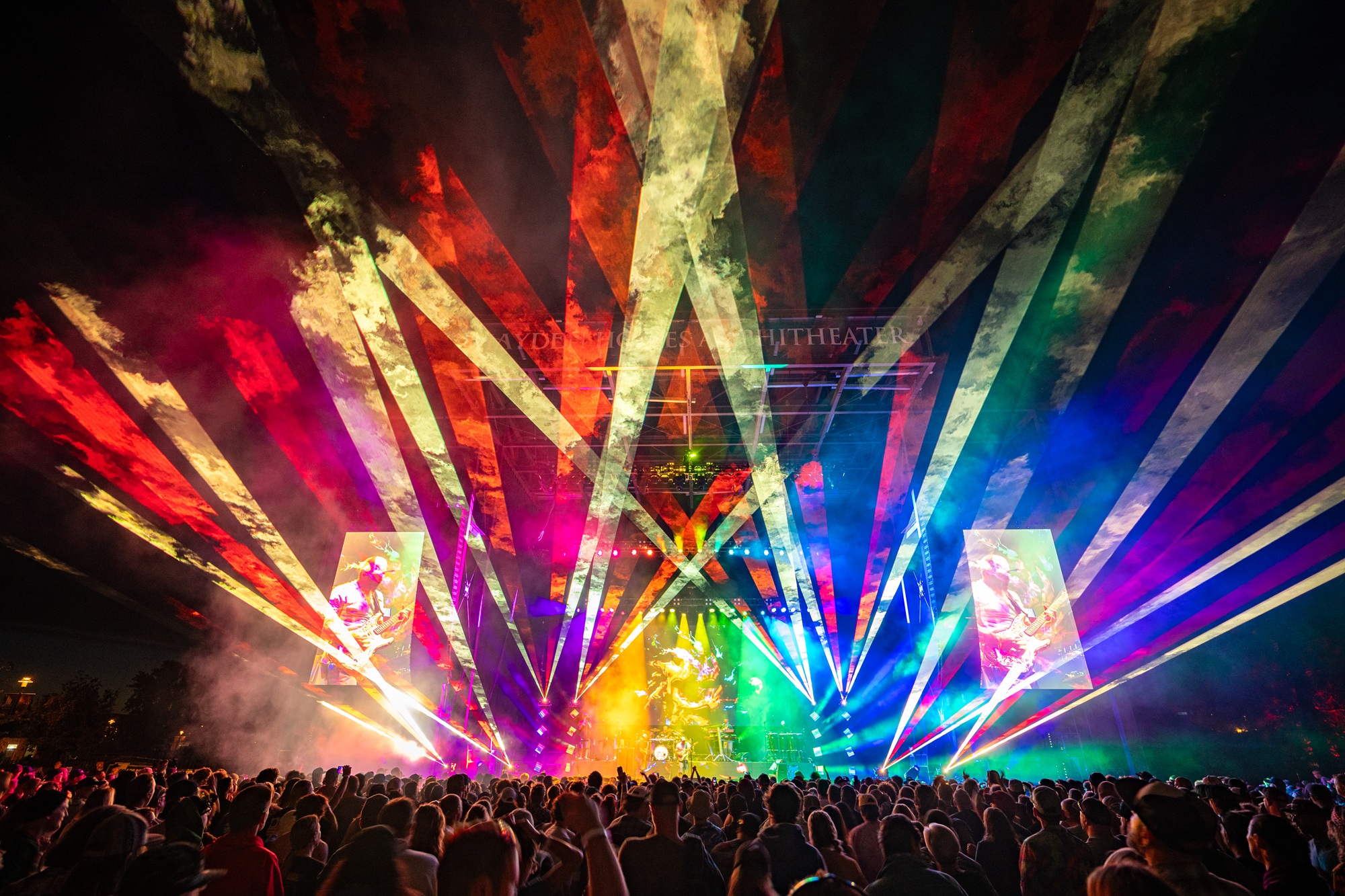 The stage of Hayden Homes Amphitheater in Bend, Oregon lit up by rainbow color laser display.