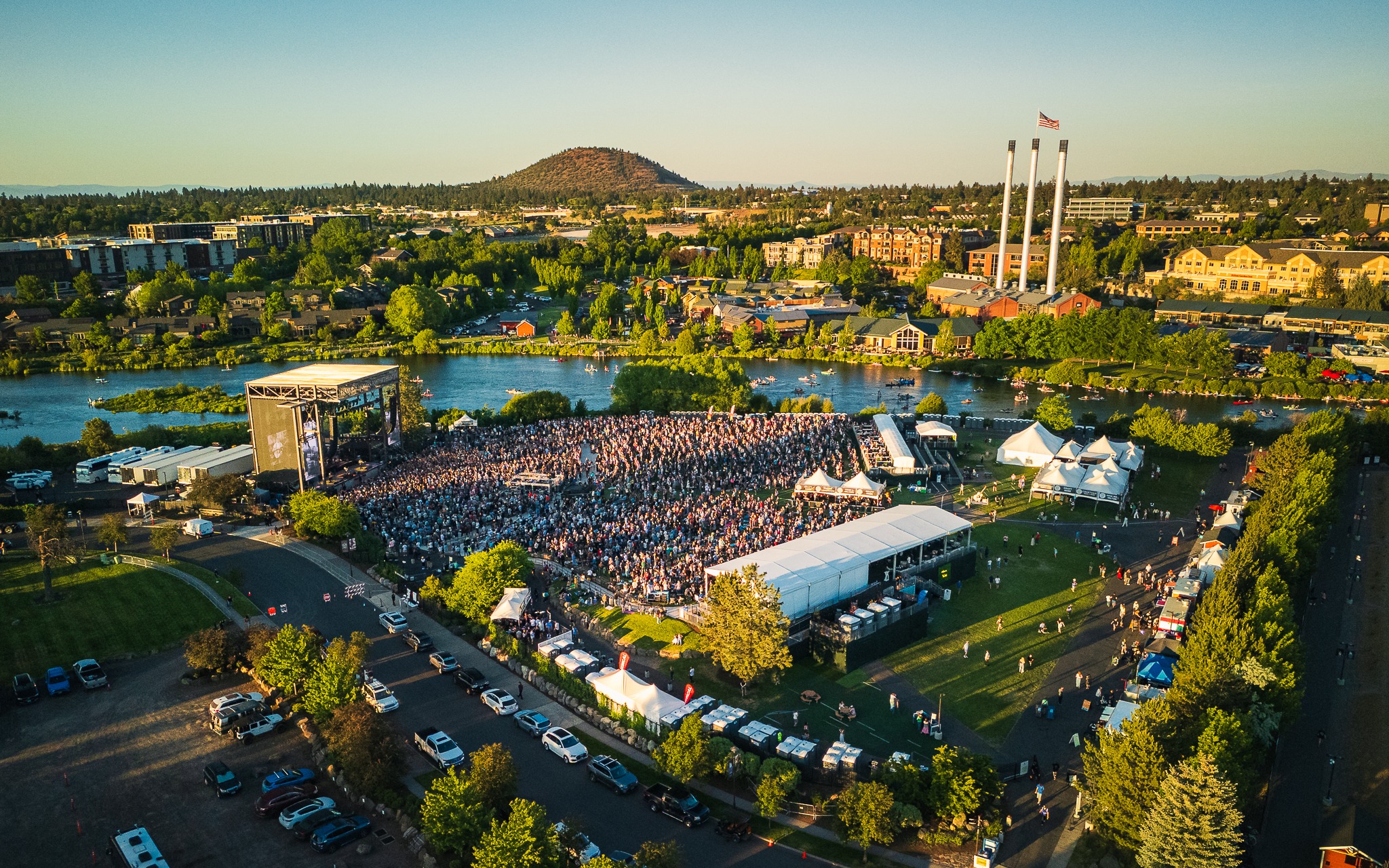 Aerial view of Hayden Homes Amphitheater in Bend, Oregon with the Deschutes River, Old Mill District stacks, and Pilot Butte in the background.