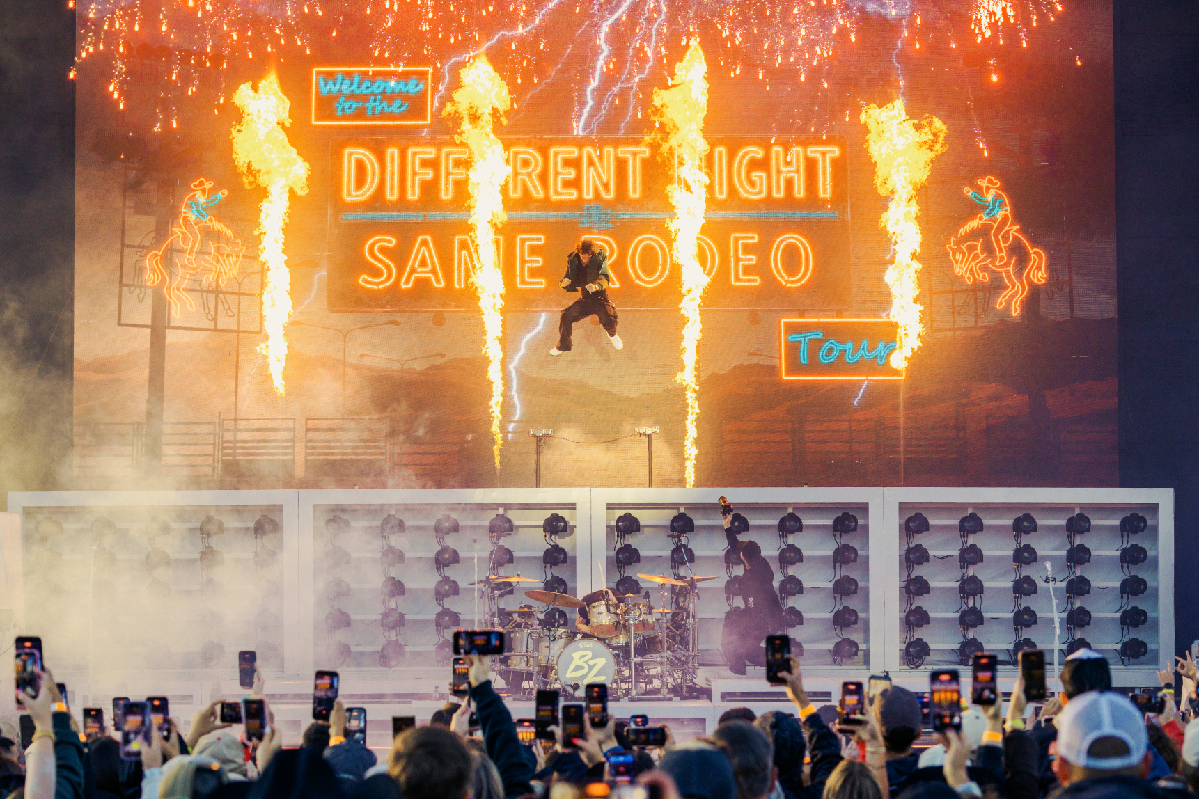 Country singer Bailey Zimmerman 15 feet in the air on stage at Hayden Homes Amphitheater in Bend, Oregon with flames and his name lit up behind him.
