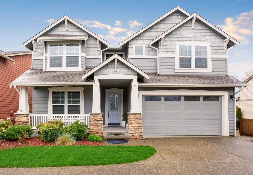 Two-story suburban house with gray siding, white trim, a front porch, and an attached two-car garage.