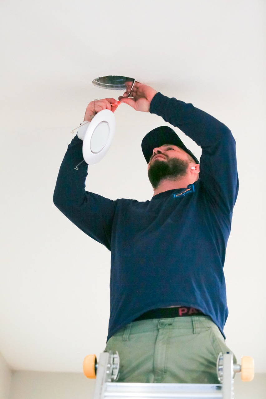 Man on ladder installing a recessed ceiling light fixture.