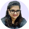 Portrait of a smiling woman with glasses and dark wavy hair wearing a dark top against a light purple background.