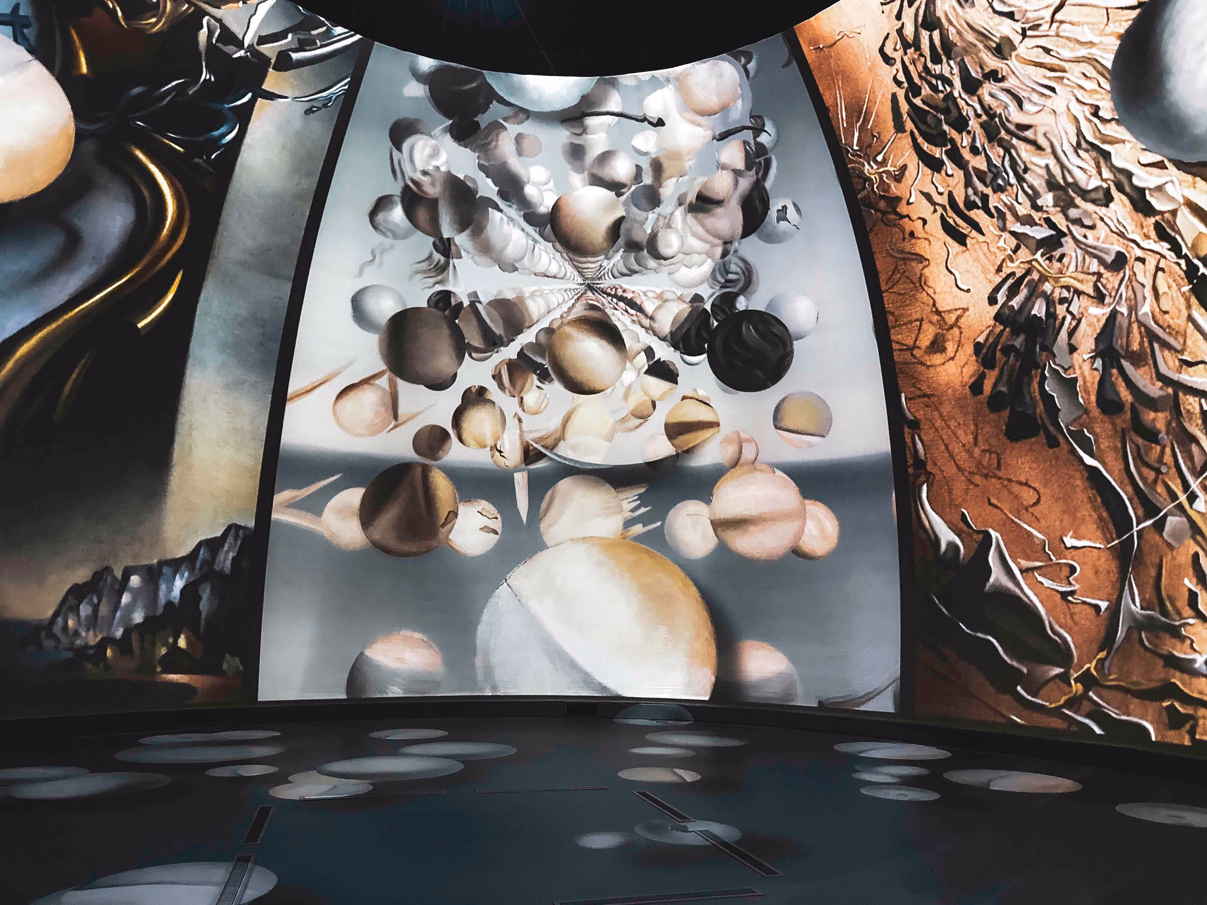 Curved room with abstract artwork featuring floating spheres and textured patterns, reflecting circular shapes on the floor.