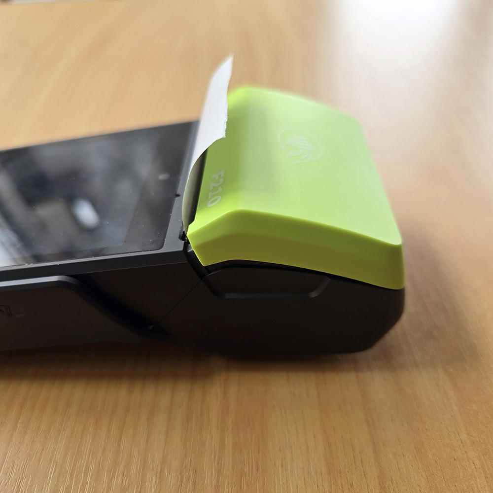 Close-up of a black and green portable thermal receipt printer with a partially printed receipt emerging.