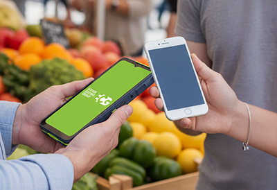 Person holding an EFTPOS machine near another person's smartphone to make payment at a market.
