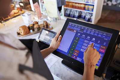 Person using touchscreen POS system at a bakery counter with pastries in the background.