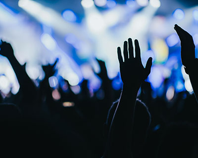 Raised hands silhouetted against bright blue stage lights at a lively concert or event.