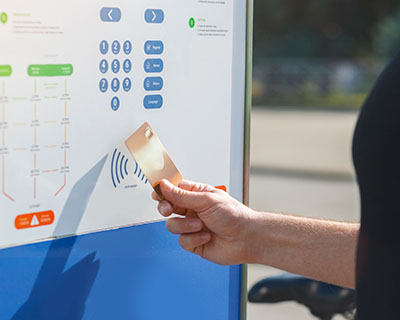 A hand holding a card near a card reader on a kiosk with instructions and icons.