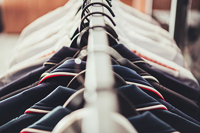Row of dark-colored suits hanging on black hangers along a clothes rack, with a blurred background.
