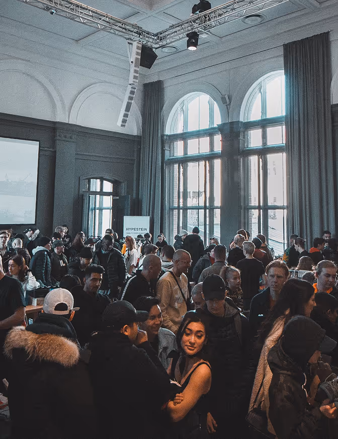 In einer Eventhalle sind viele Gäste zu sehen, welche sich zum Networking unterhalten.