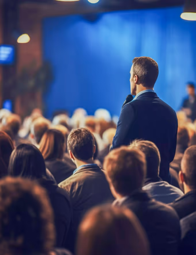 Das Publikum sitzt in einem Konferenzsaal, während ein Gast steht und eine Frage stellt.