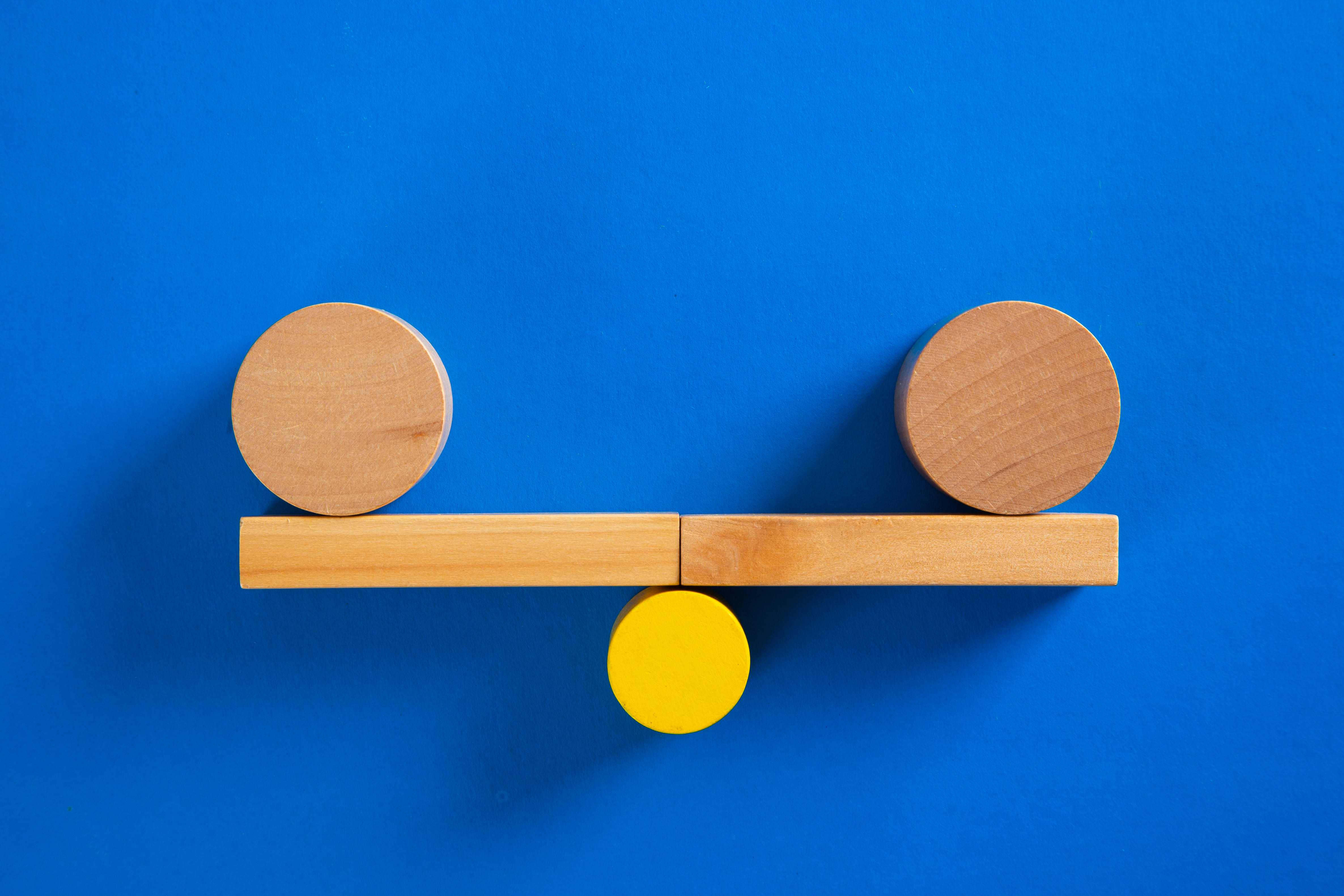 Balancierende Gewichte auf Holzbrett als Symbol für Ausgeglichenheit und Fairness