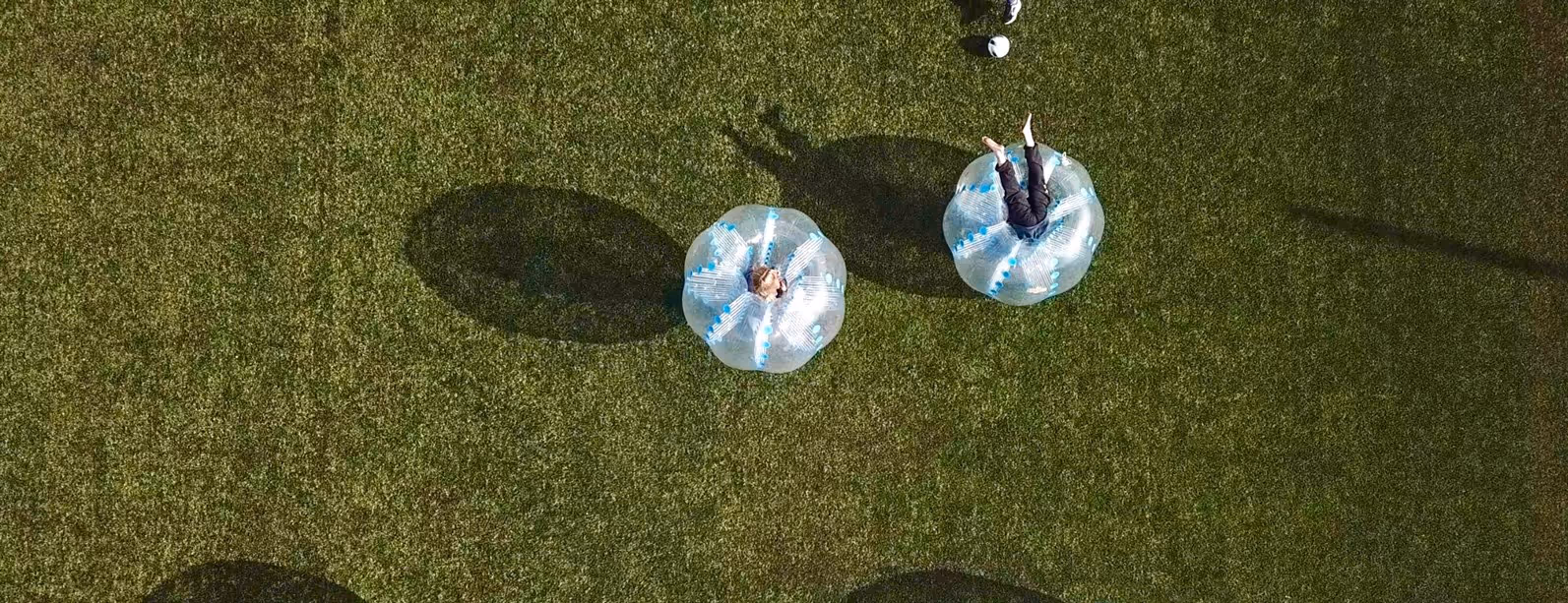 To personer i bobleballer på en fotballbane, sett fra et fugleperspektiv.