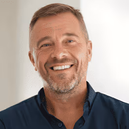 Smiling middle-aged man with short hair and beard wearing a dark blue shirt against a light background.