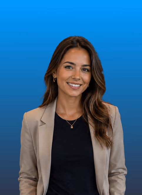 Frau mit braunem Haar, beigem Blazer und schwarzem Shirt lächelnd vor blauem Hintergrund.