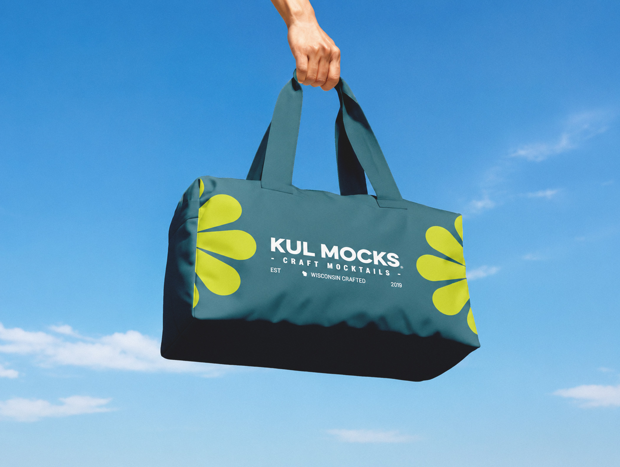 Hand holding a blue bag with yellow floral designs and KUL MOCKS craft mocktails logo.