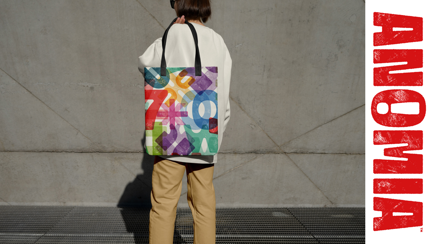 Person holding a colorful tote bag with various overlapping letters on a concrete background.