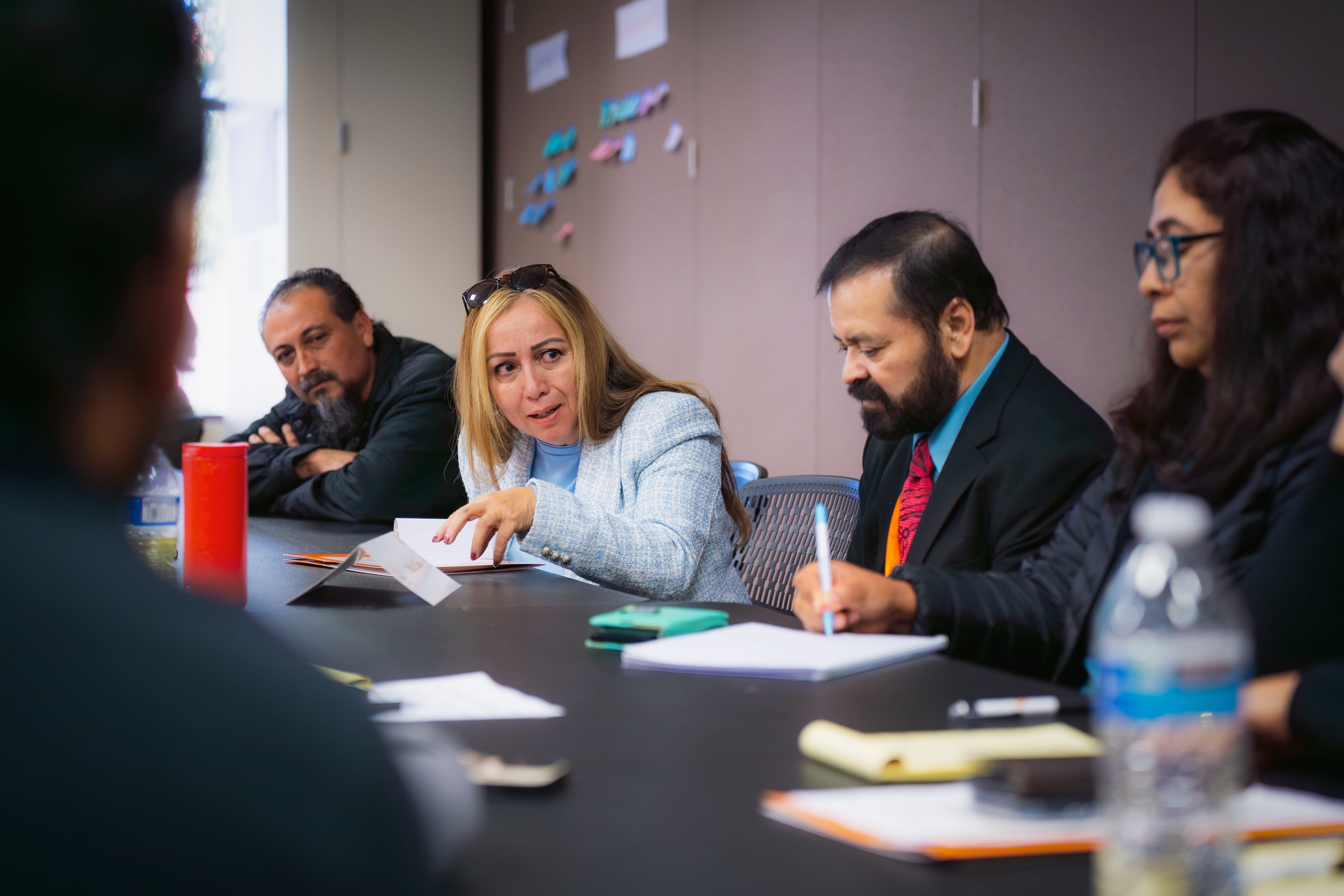 Group of professionals seated around a conference table engaged in discussion and note-taking.