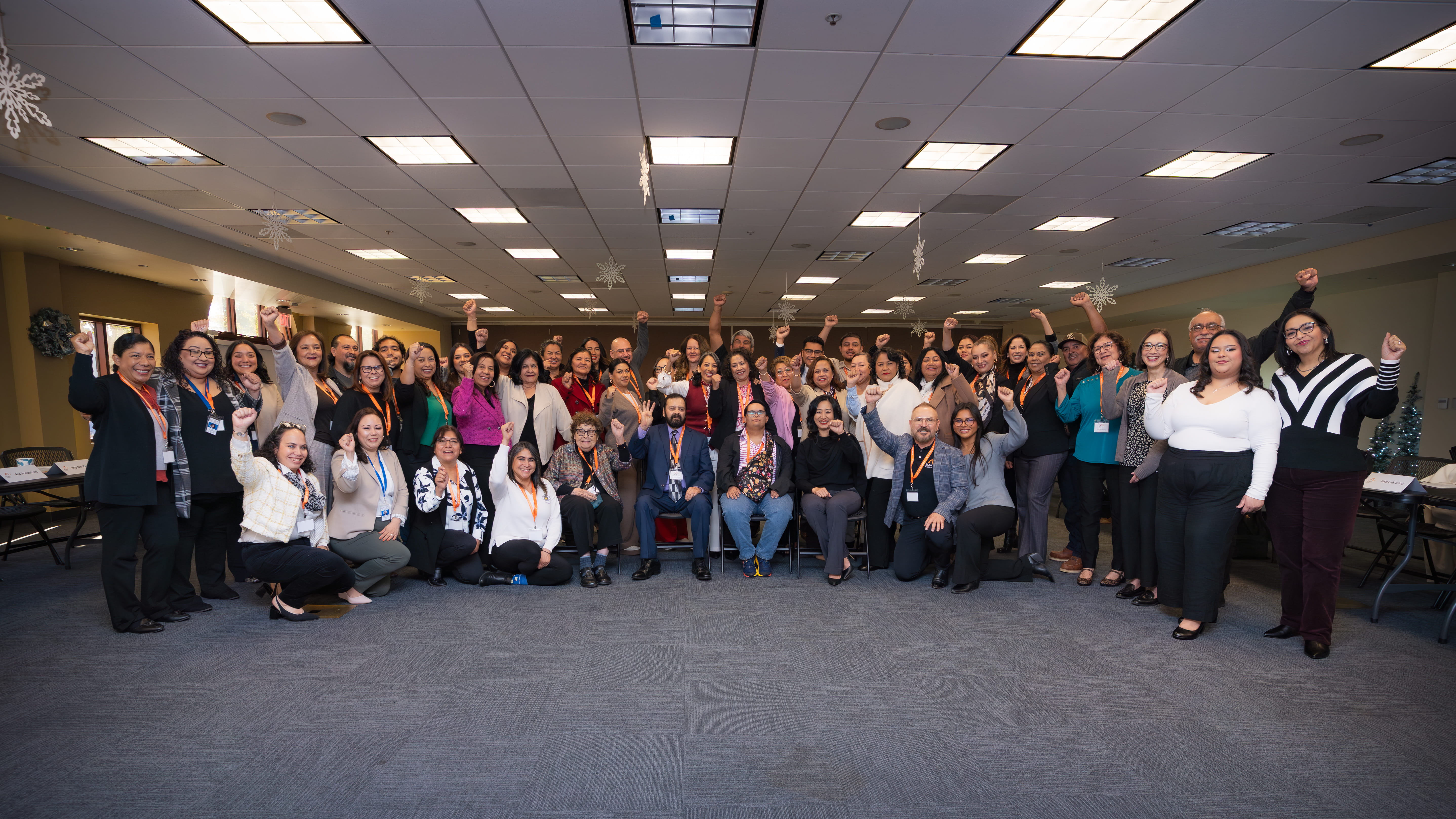 Large diverse group of people in business casual clothing posing indoors with raised fists.