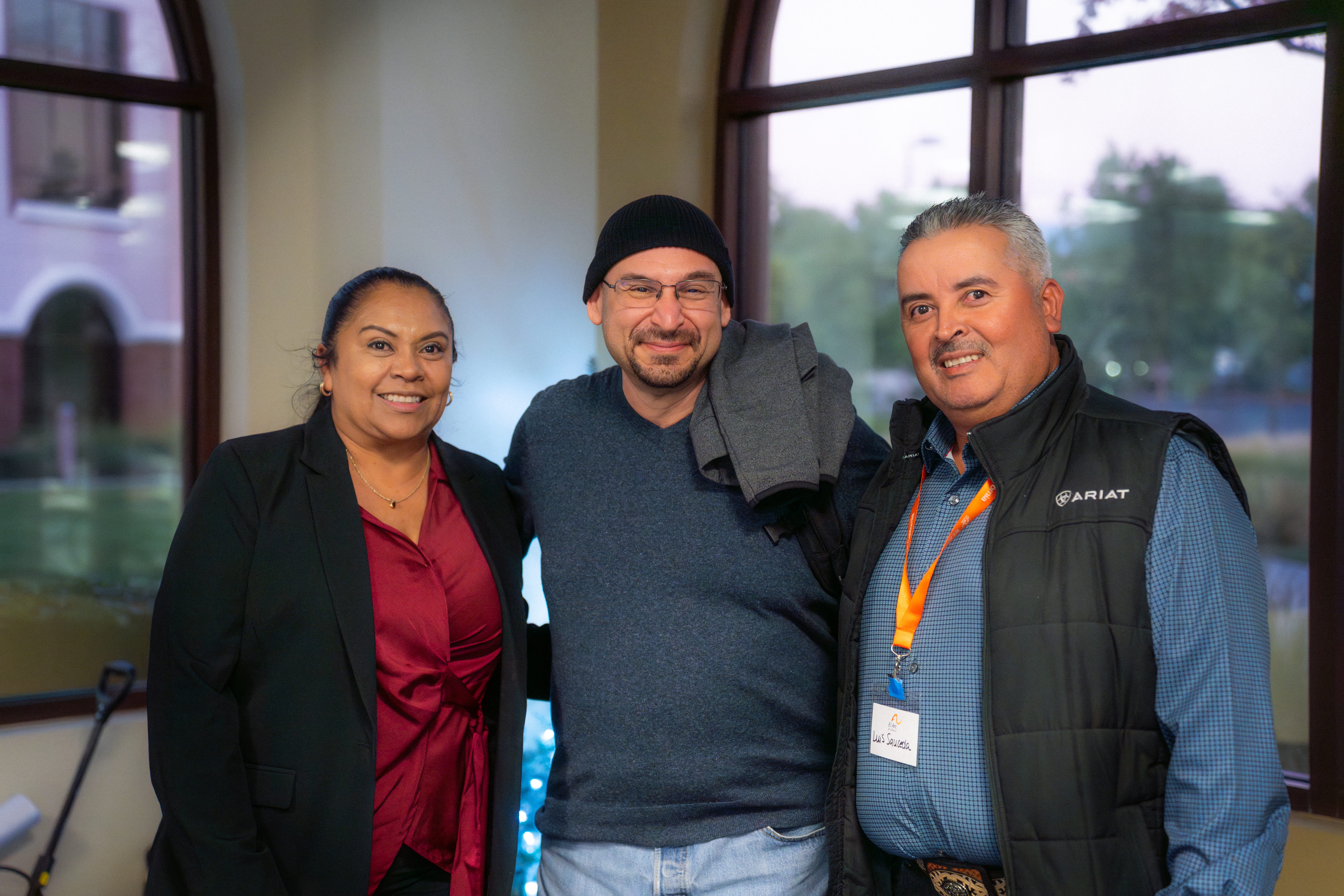 3 people in the corner of a room with glass windows taking a picture.
