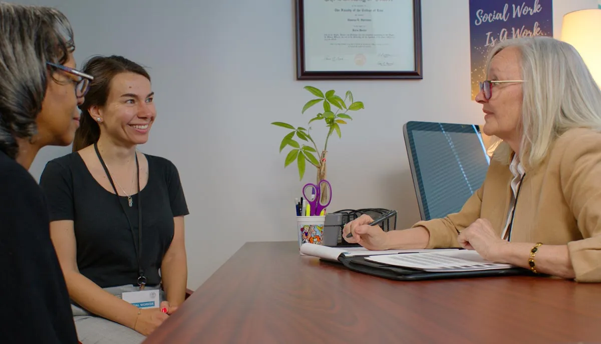 three women sitting at a desk in an office having a discussion